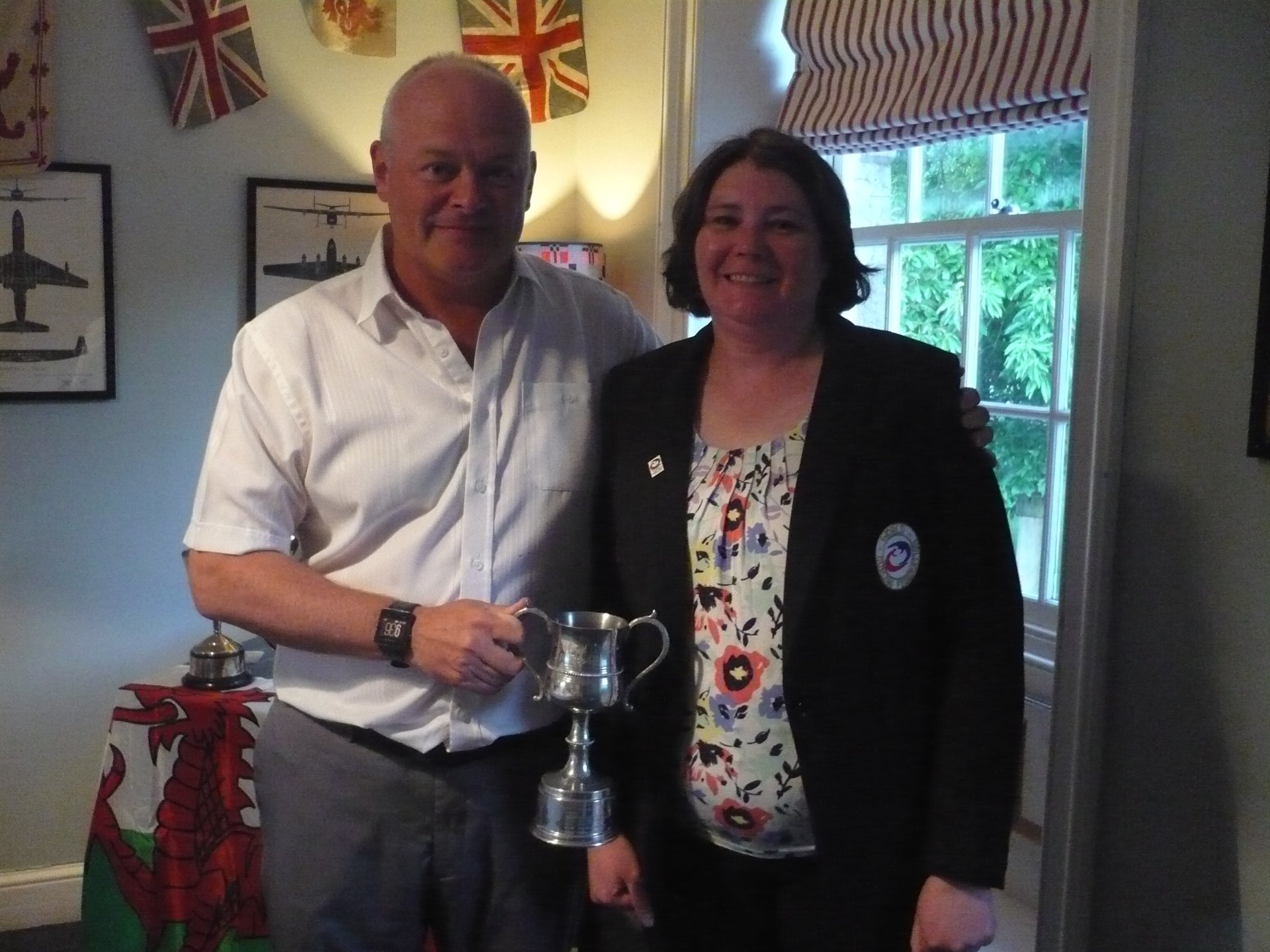 Photograph of Adrian Meikle, wearing a white shirt, handing a silver trophy to Lisa Peters, wearing a black blazer