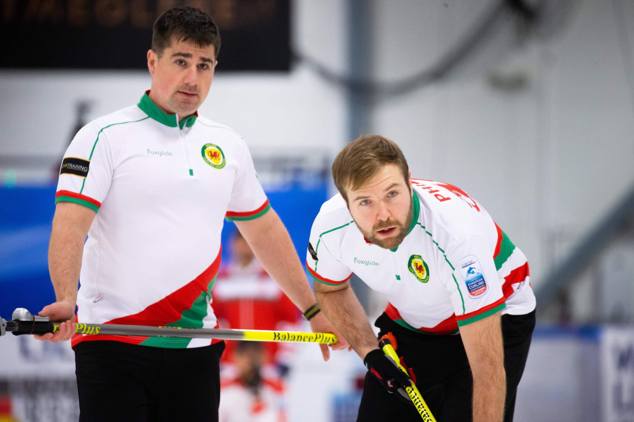 Simon Pougher and Rhys Phillips Simon Pougher and Rhys Phillips sweep a stone, wearing white kit